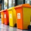 Stickers bestellenKleurrijke afvalcontainers in oranje, geel en rood met reflecterende oppervlakken tegen stedelijke achtergrond
