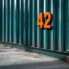 Zeecontainer met oranje huisnummer sticker "42" op donkerblauwe metalen oppervlak, geplaatst op betonnen ondergrond