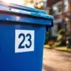 Blauwe afvalcontainer met huisnummer 23 sticker op Nederlandse woonstraat met bakstenen huizen op achtergrond
