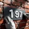Hand in werkhandschoen brengt moderne huisnummersticker aan op verweerde rode bakstenen muur