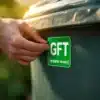 Groene GFT-sticker wordt aangebracht op schone rolcontainer in woonwijk, close-up van professionele toepassing