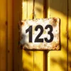 Verweerd huisnummer 123 sticker op zongebleekte houten deur met UV-schade en loslaten randen in Nederlands woongebied