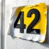 Huisnummer stickers "42" met bubbelvorming en loslating door verkeerde toepassing op witte deur