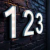Reflecterende huisnummerstickers "123" op donkere bakstenen muur, glanzend zilver-wit materiaal in avondlicht