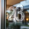 Transparante huisnummer stickers "23" op glazen voordeur van modern huis met natuurlijke lichtreflecties