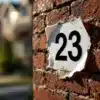 Huisnummer sticker "23" die loslaat van bakstenen muur, met zichtbare lijmresten en vuil eronder