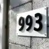Witte huisnummersticker met zwarte cijfers wordt aangebracht op getextureerde betonnen gevel van modern huis