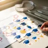 Ontwerpersdesk met kleurrijke afstudeerstickers, kalender met mei en juni maanden gemarkeerd met rode cirkels, meetlint en snijgereedschap