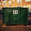 Groene afvalcontainer met huisnummersticker op Nederlandse straat met bakstenen bestrating en rijtjeshuizen