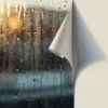 Verweerde buitensticker pelt af op regenachtig glas naast perfect gehechte binnensticker op witte muur, zonlicht creëert contrast