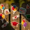 Kleurrijke verjaardag- en afstudeerstickers op verweerde houten schutting met regendruppels, heldere kleuren in ochtendlicht
